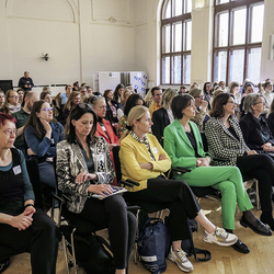 Teilnehmende, vor allem Frauen, sitzen in einem hellen Saal und hören aufmerksam einer Veranstaltung zu.