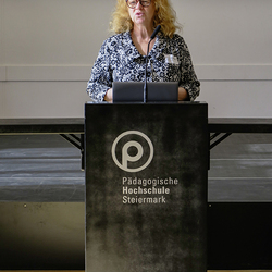 Patricia Hladschik spricht an einem Rednerpult mit Mikrofon an der Pädagogischen Hochschule Steiermark.