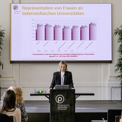 Smirna Malkoc spricht am Rednerpult der PH Steiermark. Auf der Leinwand hinter ihr ist ein Diagramm zur Frauenrepräsentation an Unis von 2010–2020 zu sehen.
