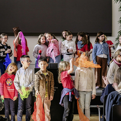 Kinderchor singt das Lied „Schmetterling“ und tanzt mit bunten Tüchern vor Publikum in einem Veranstaltungssaal.