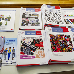Ein Tisch mit ausgebreiteten Bildungsmaterialien von Zentrum polis, die während der Mittagspause zur Verfügung stehen. Zu sehen sind Broschüren, Hefte und Flyer zu politischen und gesellschaftlichen Themen wie:  „Schulische Bubenarbeit“ mit einer Ill