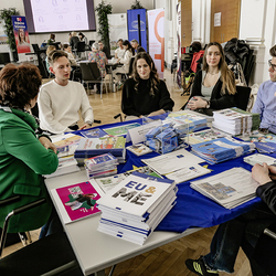Ein informativer EUROPE DIRECT Steiermark-Stand während einer Veranstaltung. Kathrin Schreiner präsentiert Materialien und Bildungsangebote für Schulen an einem Tisch, der mit einem blauen EU-Tuch bedeckt ist. Rund um den Tisch sitzen junge Erwachsen