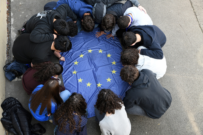 Europaflagge liegt am Boden und junge Menschen hockerln im Kreis rund um die Flagge