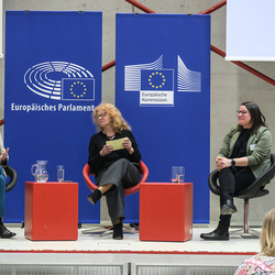 Podiumsdiskussion mit Petra Stolba, Agnes Gotthardt, Moderation Patricia Hladschik, im Hintergrund Rollups vom Europäischen Parlament und der Europäischen Kommission