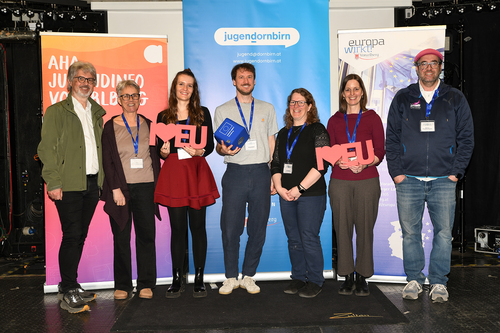 Organisationsteam (4 Frauen, drei Männer) steht nebeneinander auf einer Bühne